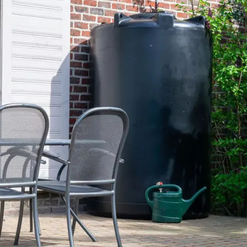 Citerne eau de pluie en plastique noir de forme ronde, placée sur une terrasse contre un mur en briques.